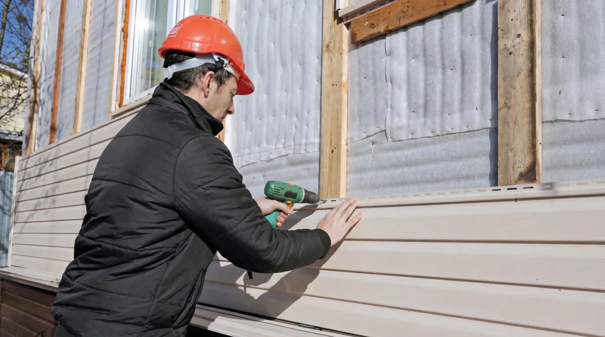Siding replacement professional using a power drill to install new tan vinyl siding on a home exterior in Bellevue, WA
